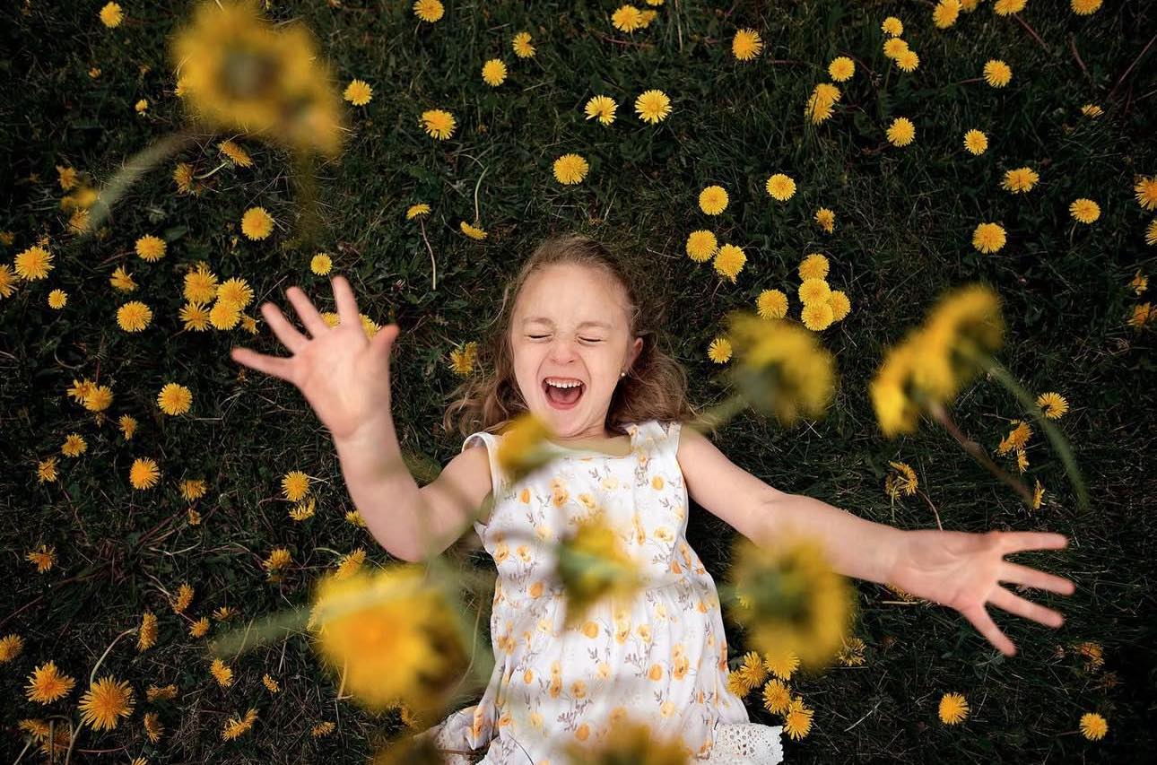 young child laughing in grass and yellow flowers