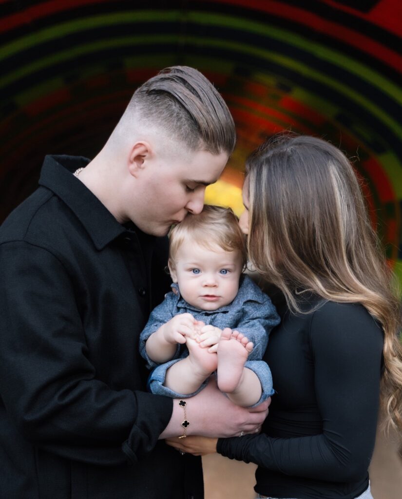 Family of three, parents kissing their baby on the head