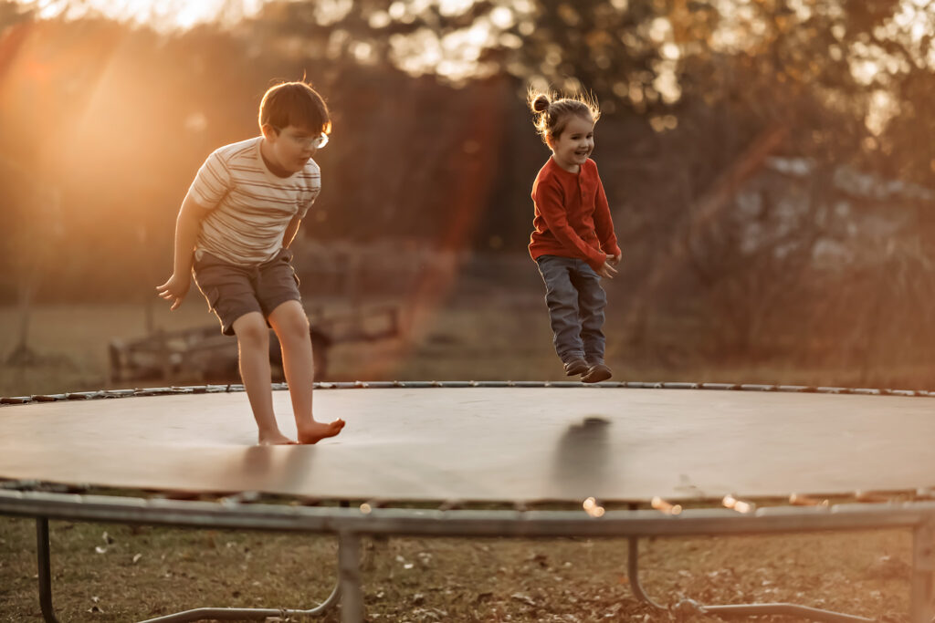 two young siblings jumping on a trampoline