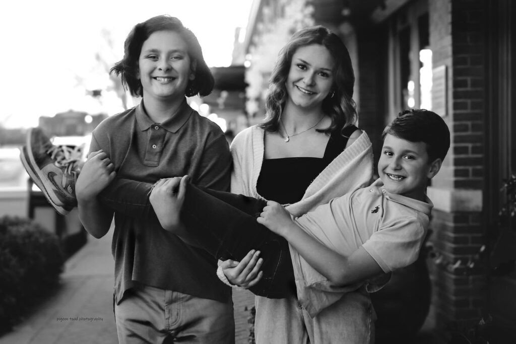 two siblings holding third sibling all smiling