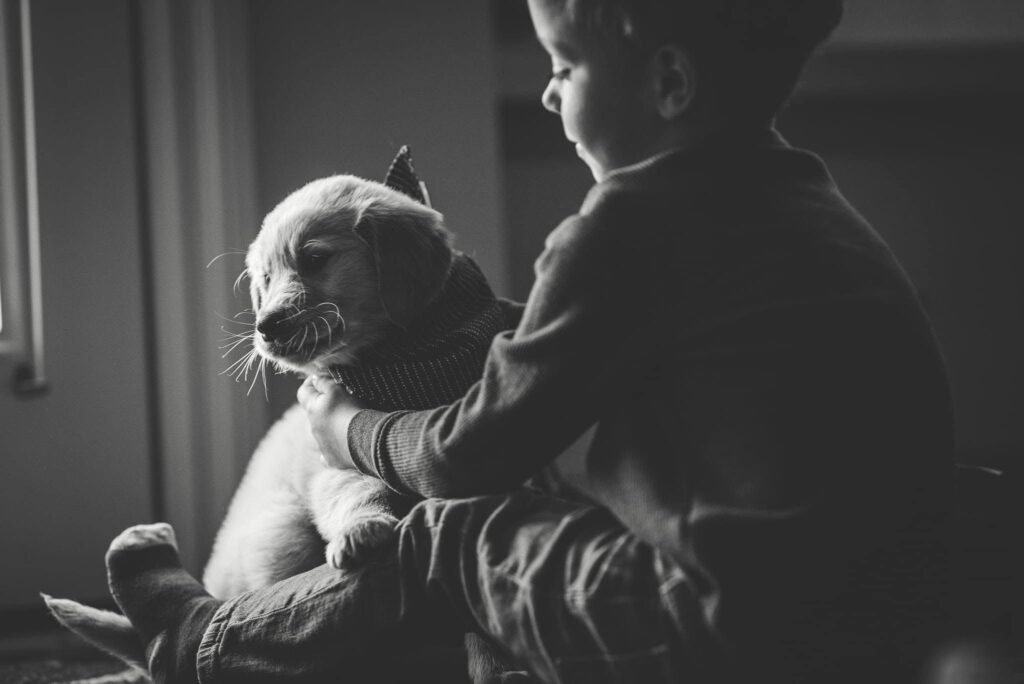 Child sitting by the window looking down and smiling and their puppy