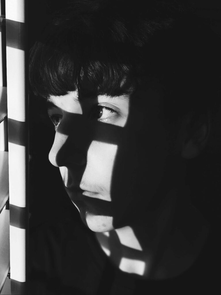 Black and white image of you adult looking outside with harsh shadows on face