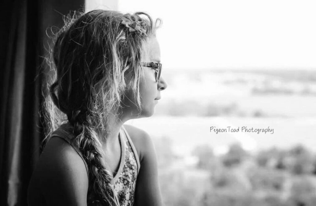 Child sitting by the window and looking outside in black and white