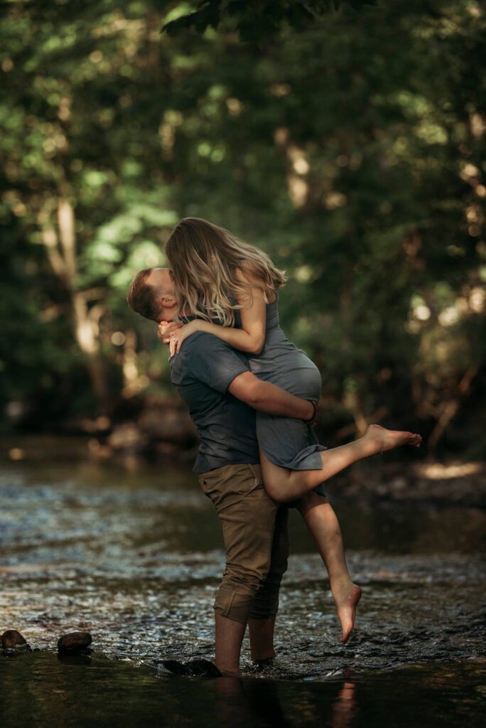 Couple kissing standing in river, forest area with dappled light