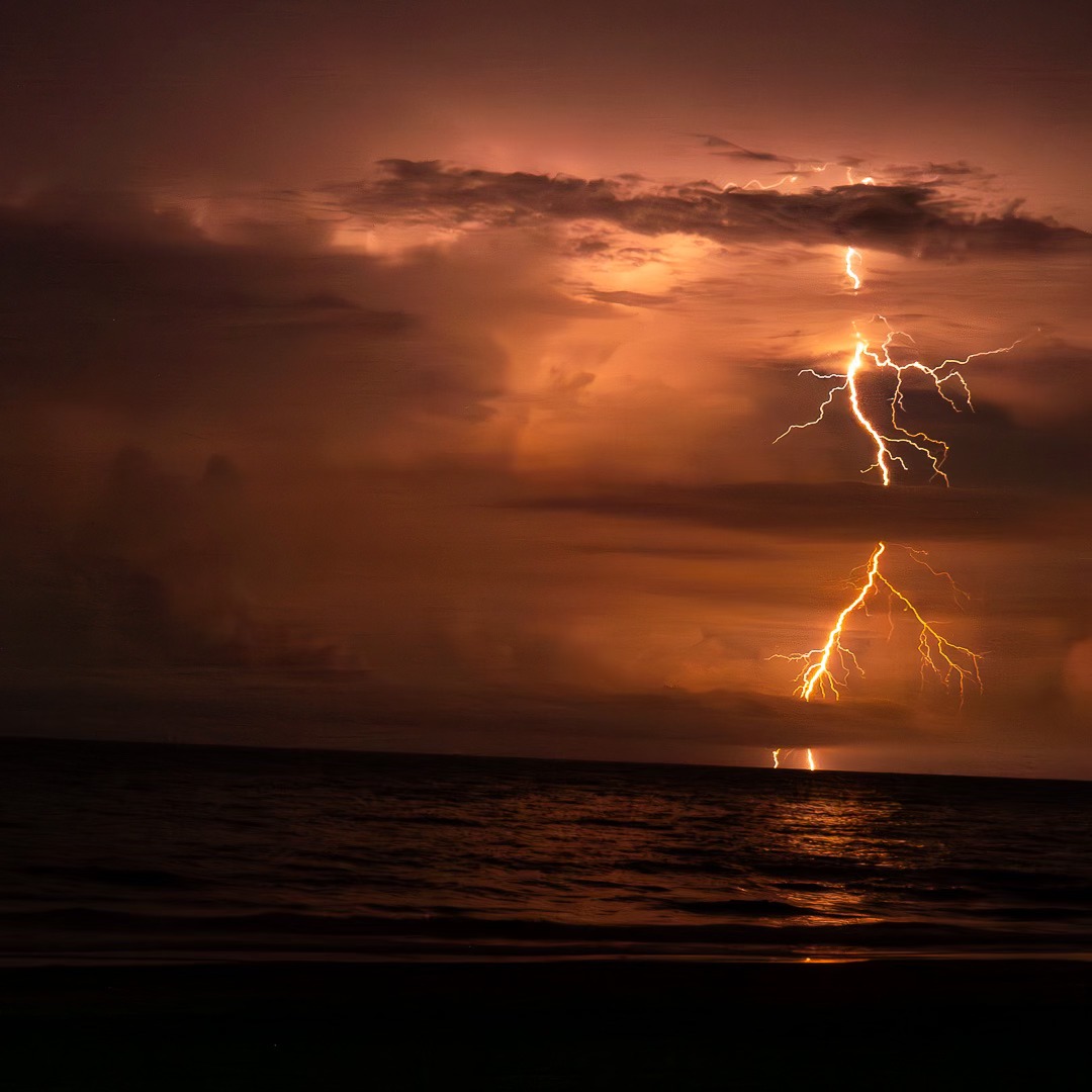 lightning storm at sunset over body of water
