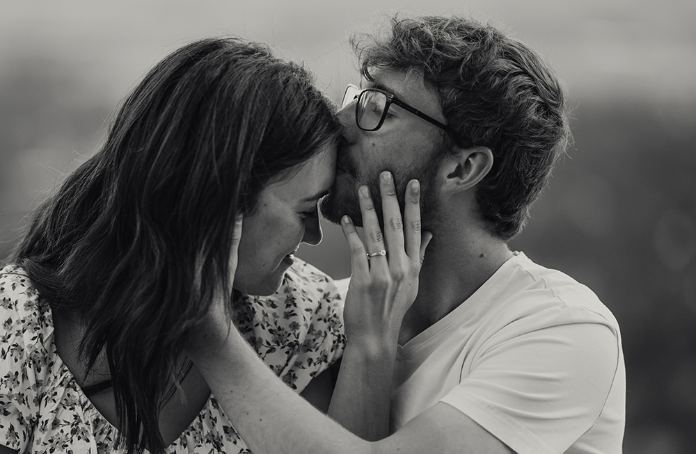 portrait of engaged couple showing off ring with a kiss on forehead