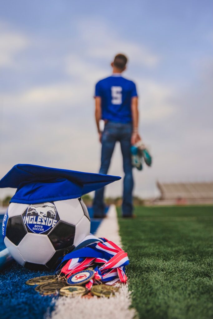 up close shot of soccer ball, graduation cap, and medals with student standing a long distance away
