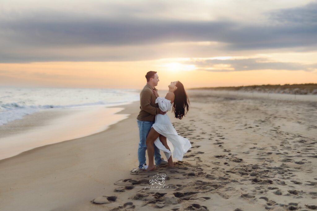A man and woman holding each other and laughing at sunset on the beach