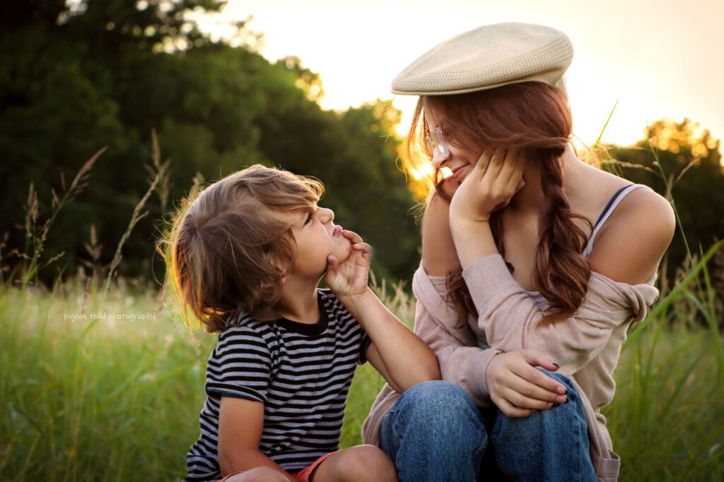 siblings making silly faces at each other sitting in grass with backlight