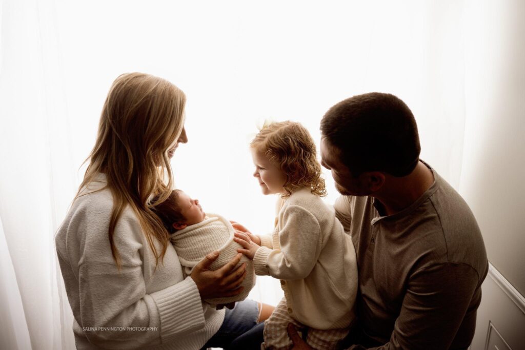backlight / window light silhouette of family of four looking at newborn